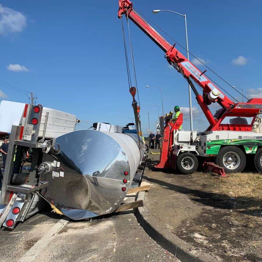 Red heavy-duty wrecker lifting an overturned tanker trailer