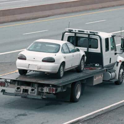 Flatbed tow truck carrying a white sedan on a highway