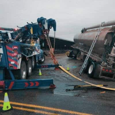 Heavy-duty wrecker recovering a tanker truck on a wet road